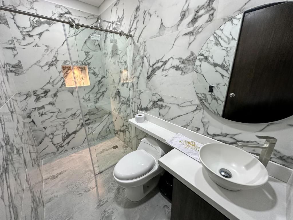 A bathroom with a marble wall, a white toilet, a white sink, and a mirror.