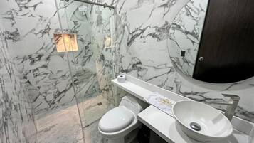A bathroom with a marble wall, a white toilet, a white sink, and a mirror.