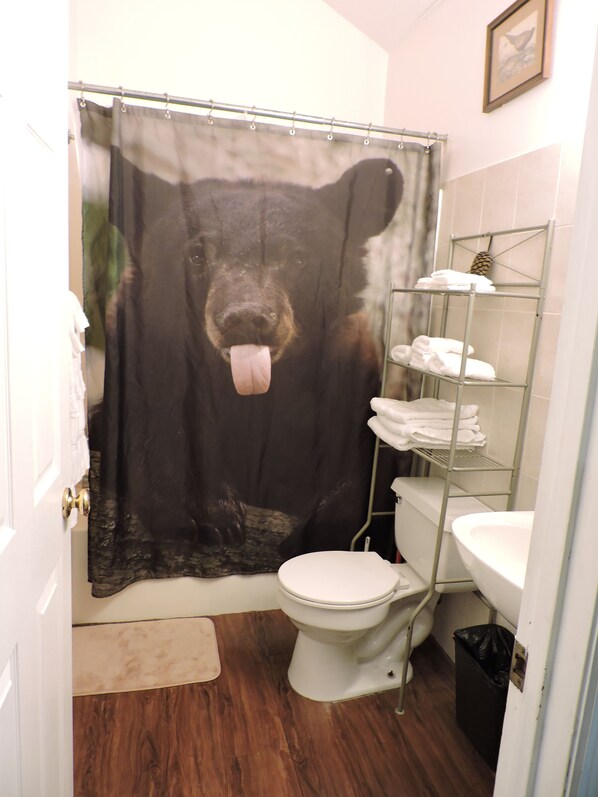 Un baño con cortina de ducha temática de oso, inodoro, lavabo y toallero.