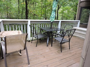 A wooden deck with a table and chairs, surrounded by a white railing, overlooking a forested area. - Tranquil 3-bedroom cabin with lots of wildlife. (Pigeon Forge)