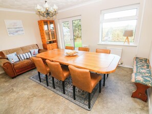 A dining area with a wooden table and chairs, a sofa with cushions, a patterned rug, and a view through a glass door. - Castle Grove (Milford Haven)