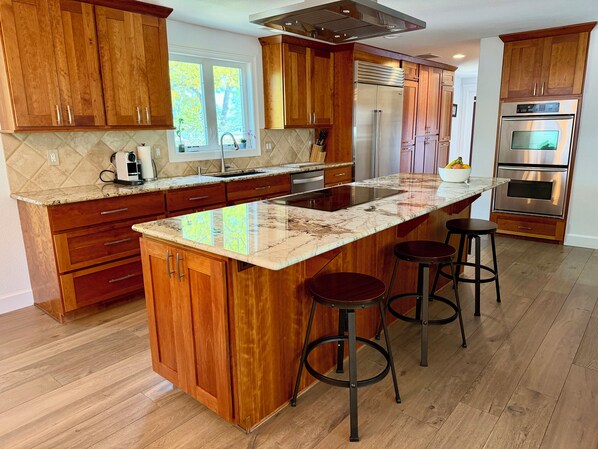 Cocina con armarios de madera, una isla grande con taburetes, horno empotrado y ventana con vistas.