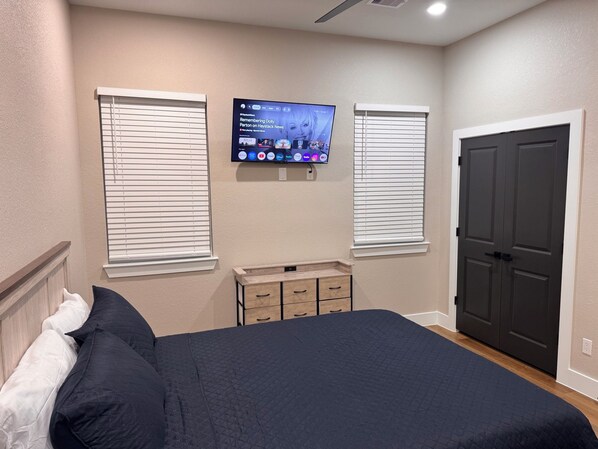 Een slaapkamer met een bed, een dressoir, een aan de muur bevestigde televisie en een deur.