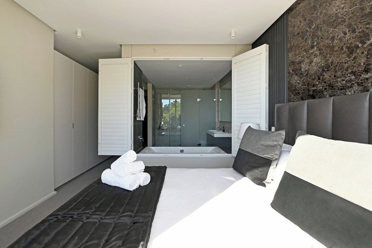 A modern bedroom with a large bed, a separate sitting area, and a view of a bathroom and outdoor area.