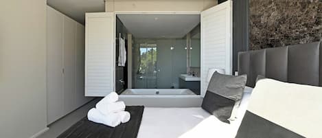 A modern bedroom with a large bed, a separate sitting area, and a view of a bathroom and outdoor area.