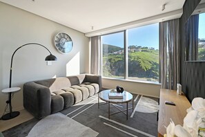 Ein modernes Wohnzimmer mit einer Couch, einem runden Couchtisch, einer Stehlampe und einem großen Fenster mit Blick auf eine grüne Landschaft.