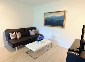 A modern living room with a black leather sofa, a white coffee table, a framed landscape painting, and a flat-screen TV. - Bright apartment at the heart of Kópavogur (Kópavogur)