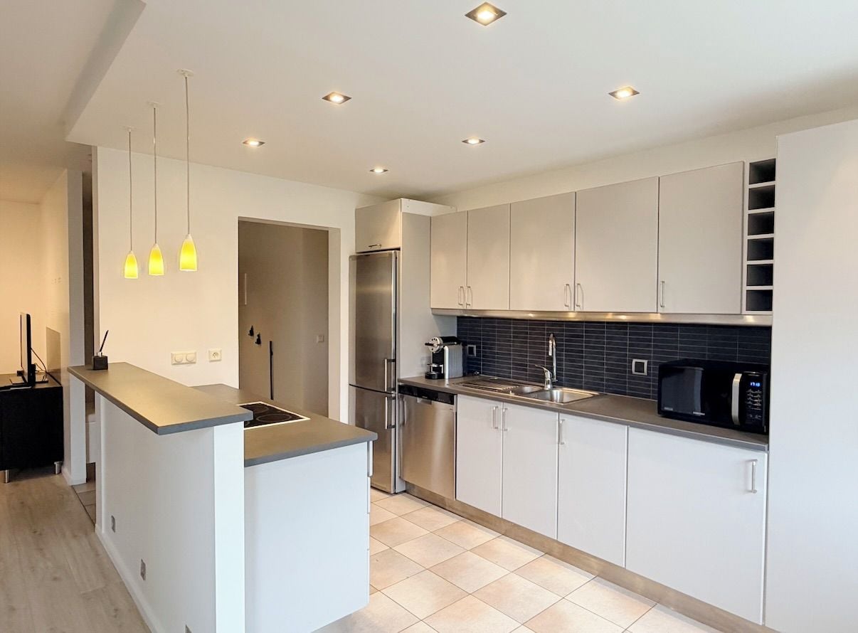 Una cocina moderna con gabinetes blancos, un refrigerador de acero inoxidable, un microondas negro y luces colgantes.