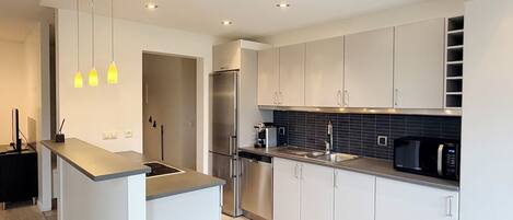 Una cocina moderna con gabinetes blancos, un refrigerador de acero inoxidable, un microondas negro y luces colgantes.