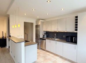 A modern kitchen with white cabinets, a stainless steel refrigerator, a black microwave, and pendant lights. - Bright apartment at the heart of Kópavogur (Kópavogur)
