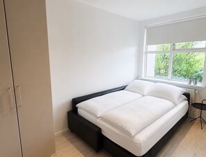 Ein Schlafzimmer mit einem Bett, einem Fenster mit Blick auf Grünflächen und einem Kleiderschrank.