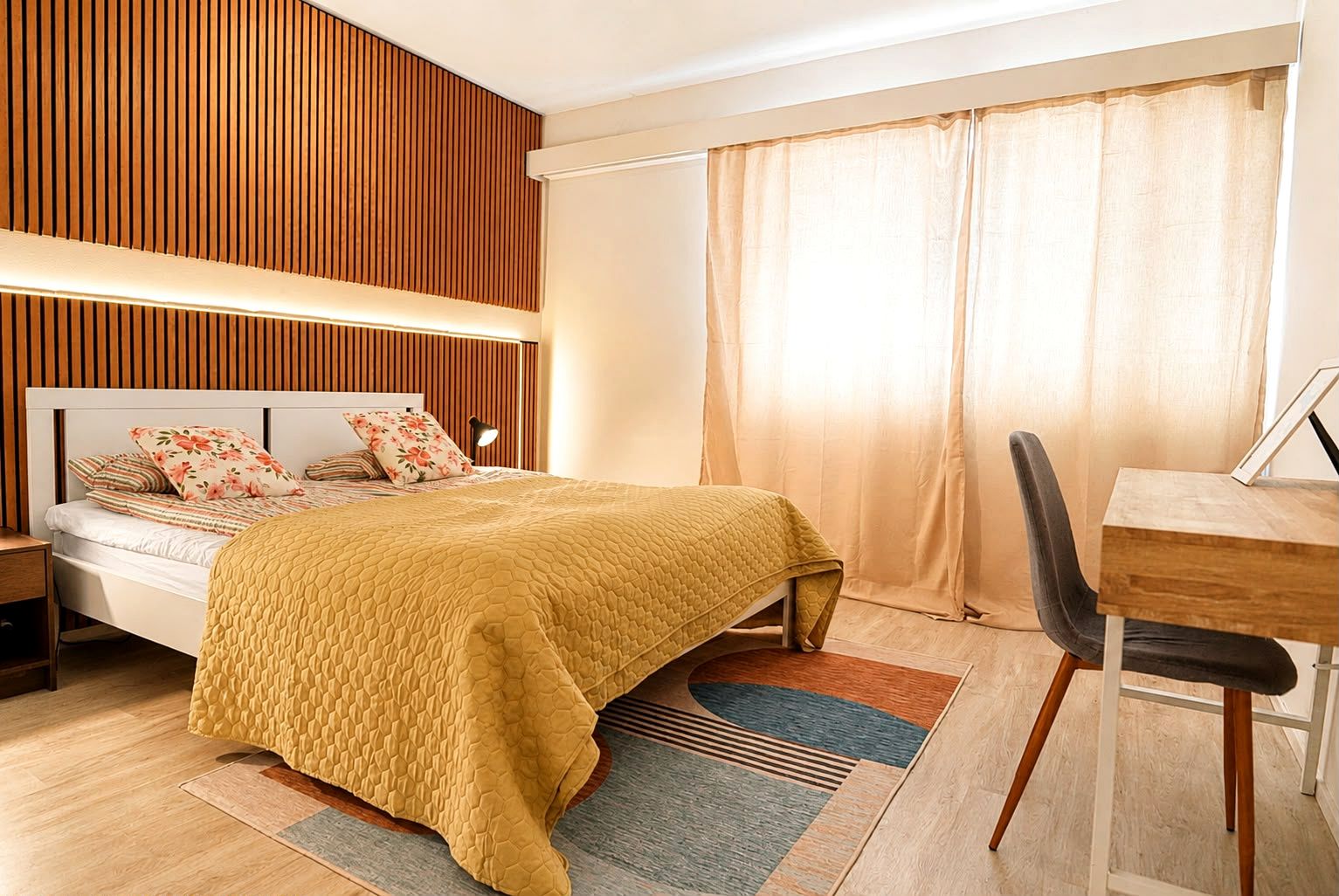 A modern bedroom with a bed, bedside table, and a desk with a chair.