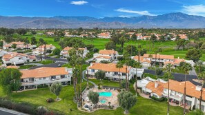 A residential area with houses featuring red-tiled roofs, surrounded by greenery and palm trees, with mountains in the background. - Desert Falls 2 Bedroom Condo (Palm Desert)