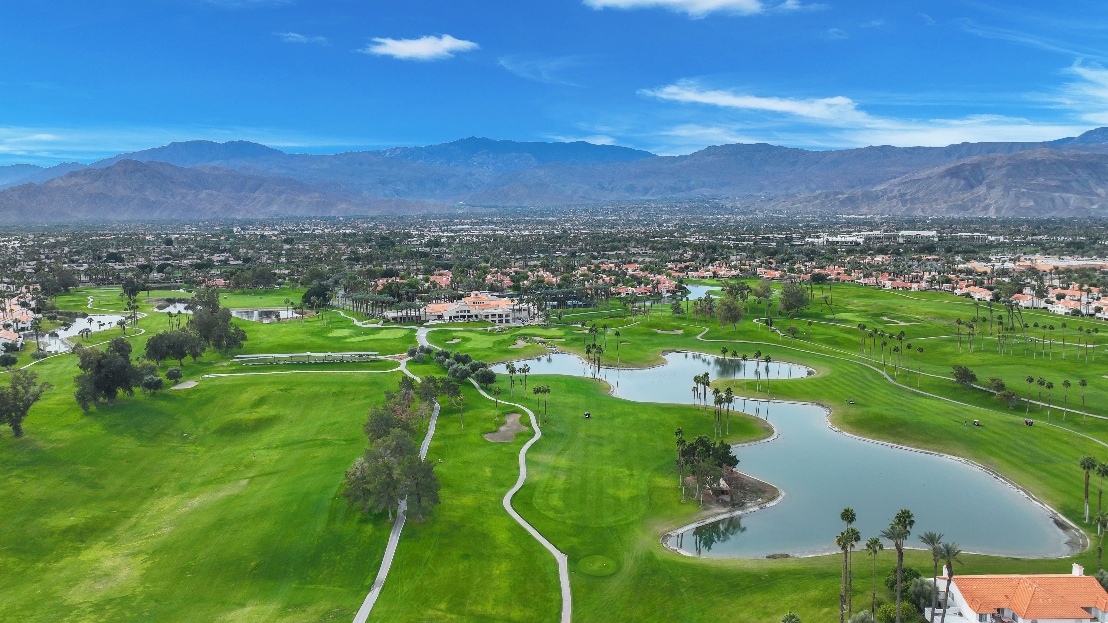 Un parcours de golf avec un étang, entouré de zones résidentielles et de montagnes.