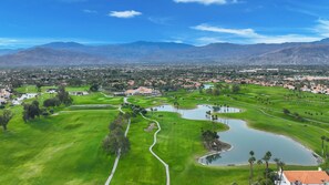 A golf course with a pond, surrounded by residential areas and mountains. - Desert Falls 2 Bedroom Condo (Palm Desert)