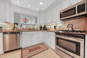 A modern kitchen with white cabinets, stainless steel appliances, and a patterned rug. - Desert Falls 2 Bedroom Condo (Palm Desert)