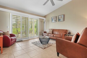 A living room with a red sofa, a brown leather couch, a glass coffee table, and a large sliding glass door leading to a balcony. - Desert Falls 2 Bedroom Condo (Palm Desert)