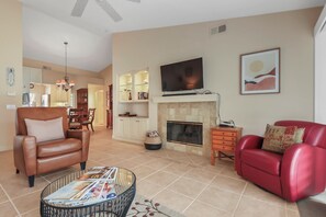 A living room with a fireplace, a television, and a dining area in the background. - Desert Falls 2 Bedroom Condo (Palm Desert)