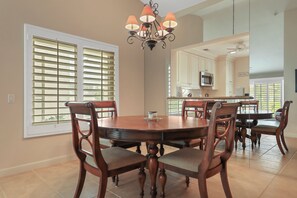 A dining area with a round wooden table, six chairs, and a chandelier. - Desert Falls 2 Bedroom Condo (Palm Desert)