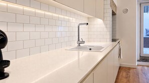 Eine moderne Küche mit weißen, im Kachelmauerwerk-Stil angeordneten Fliesen, einem Edelstahlarmaturen und einer eleganten Arbeitsplatte.