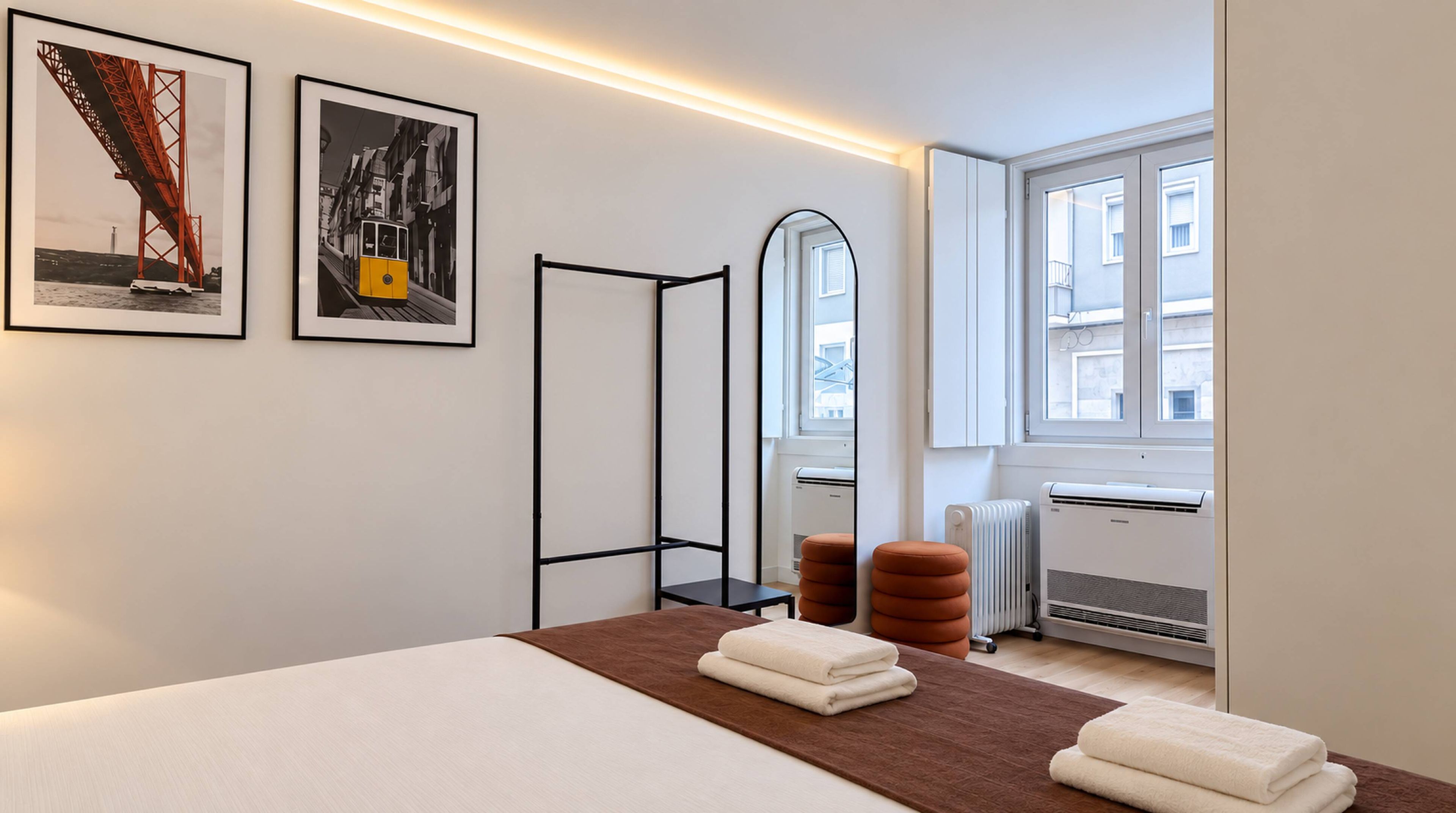 A hotel room with a bed, a radiator, a window, and two framed pictures on the wall.