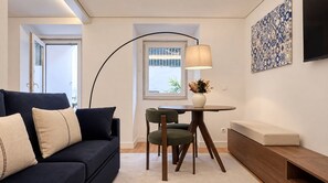 A modern living room with a dark sofa, a round table with chairs, a lamp, and a wall-mounted TV. - VIVA Lapa Serviced Apartments (Lisboa)