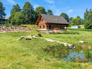 A wooden cabin with a sloped roof, a small deck, and a pond in the foreground.