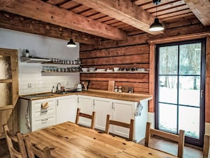 Interior de una cabaña de madera con cocina, mesa y sillas.