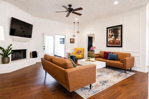 A living room with a fireplace, two sofas, a coffee table, and a ceiling fan. - Artsy Retreat: 3BR Home - King Bed, 2-Car Garage, Patio + Firepit (Lubbock)