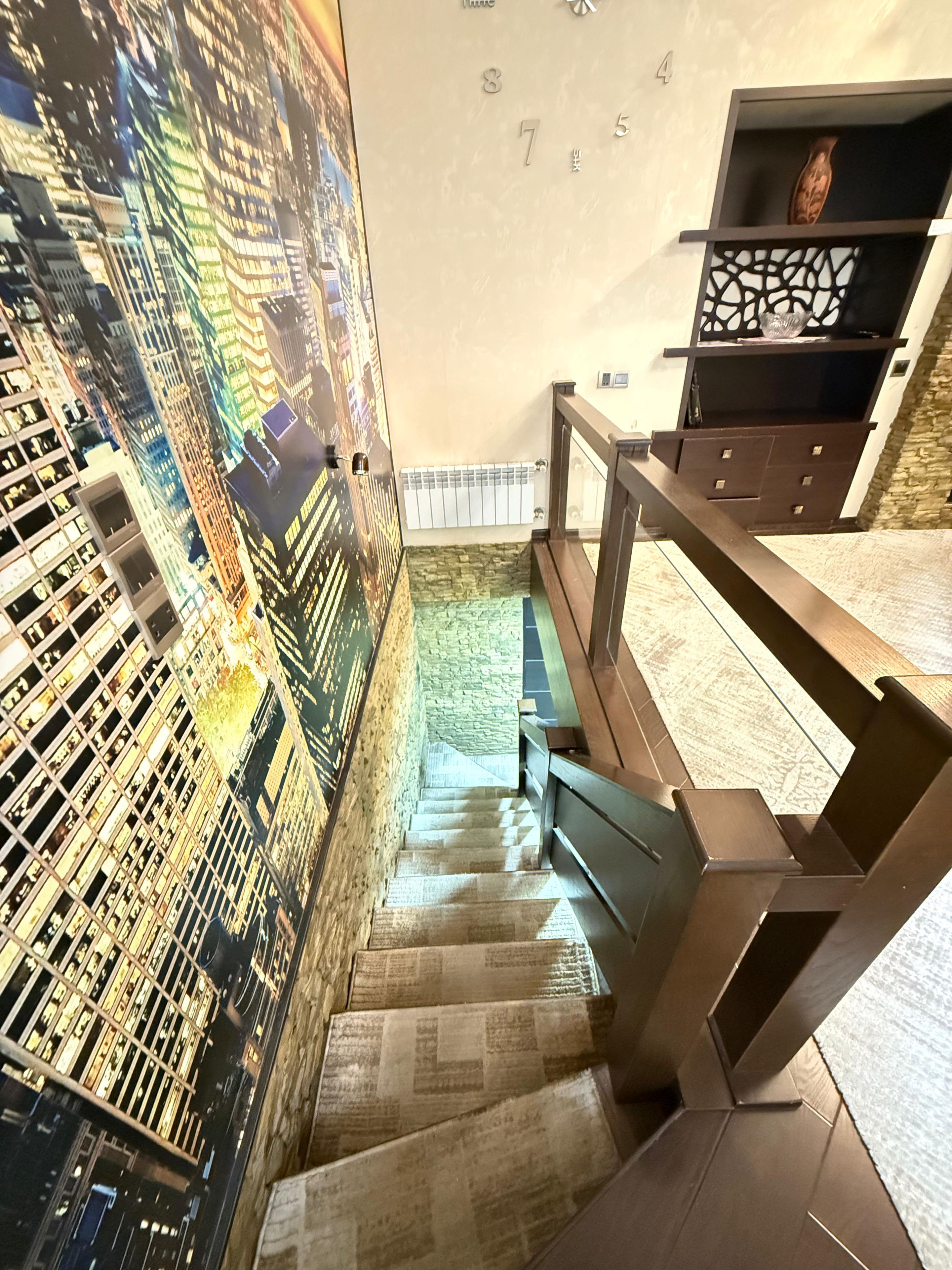 Eine Treppe mit Stadtbild-Mural an der Wand, einem Holzhandlauf und einer Steinwand mit Radiator.
