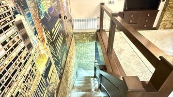 Eine Treppe mit Stadtbild-Mural an der Wand, einem Holzhandlauf und einer Steinwand mit Radiator.