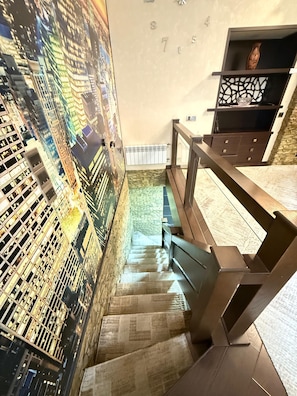 Een trap met een stadsmuur op de muur, een houten leuning en een stenen muur met een radiator.