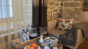 A cozy living room with a stone wall, a sofa with floral pillows, a coffee table with a tray of snacks, a book, and a vase with a plant.