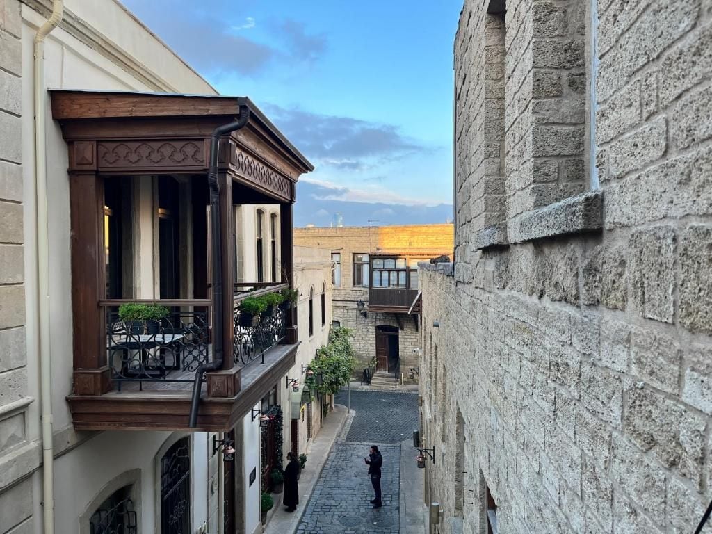 A narrow street with buildings on either side, a person walking, and a clear sky.