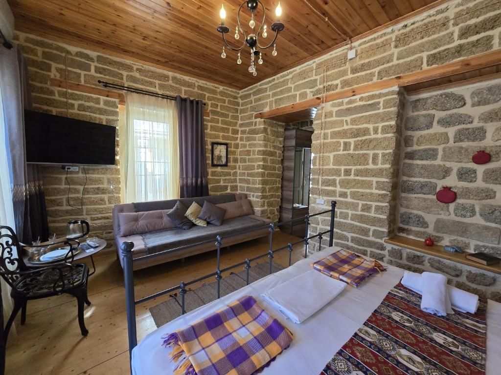 A room with a stone wall, a sofa, a bed with a patterned bedspread, a chandelier, and a flat-screen TV mounted on the wall.