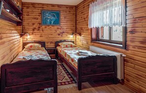 A wooden cabin room with two beds, a radiator, a window with lace curtains, and a painting on the wall. - Gorgeous home in Plaski with private swimming pool, can be inside or outside (Plaski)