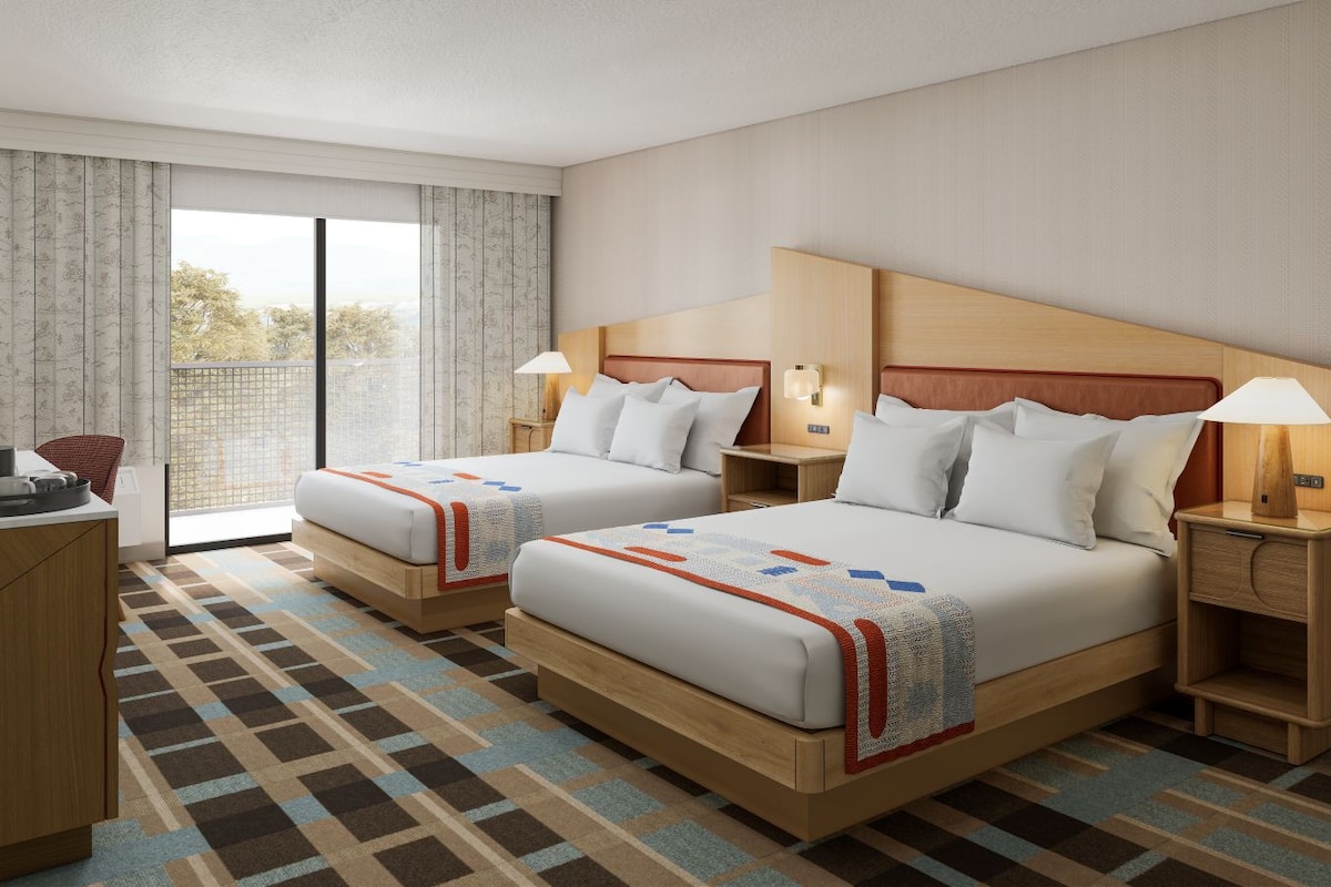 Een hotelkamer met twee bedden, een bureau en uitzicht door een groot raam.