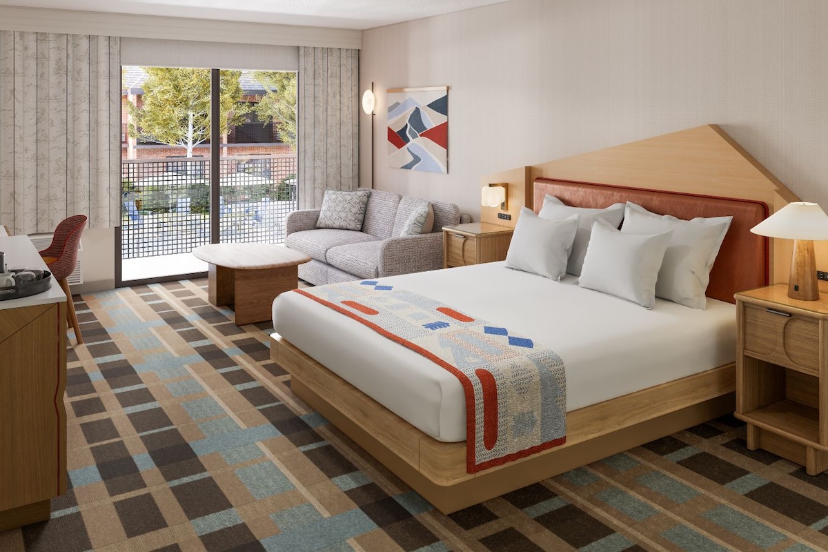 Een hotelkamer met een groot bed, een bank, een bureau en uitzicht op het omliggende landschap.