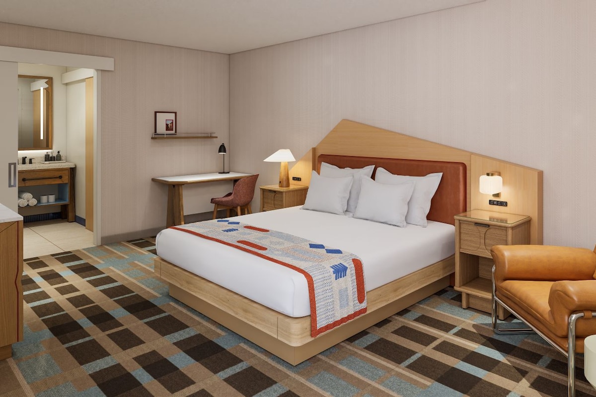Een hotelkamer met een bed, bureau, stoel en een klein tafeltje met een lamp.