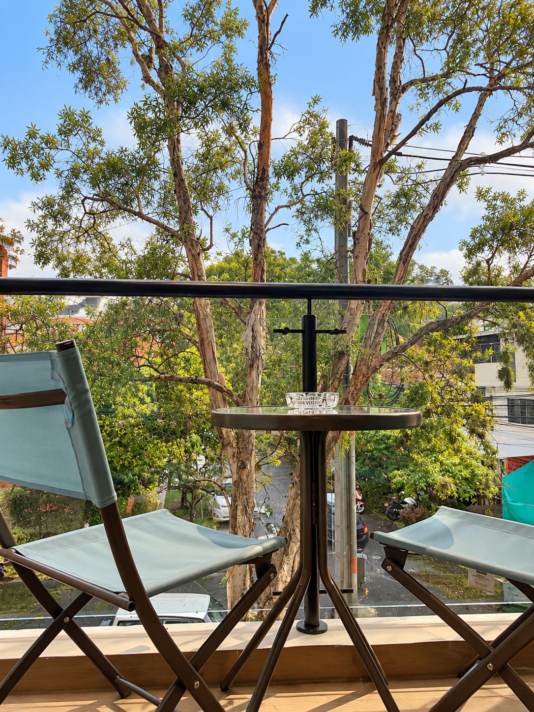 A balcony with two foldable chairs, a small round table with a glass top, and a metal railing.