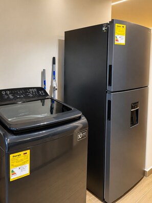 A compact kitchen with a black refrigerator and a washing machine. - 201- A/C • Balcony • 2 Workspaces • Washing Machine • Unicentro (Medellín)