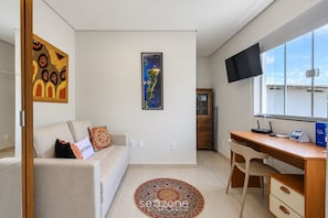 Ein modernes, helles Zimmer mit einer Couch, einem Schreibtisch, einem Fernseher und einem Fenster mit Blick.