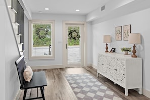 A hallway with a checkered floor, a bench, a white console table with decorative panels, and two doors leading outside. - The Lookout at Betty (Santa Rosa Beach)