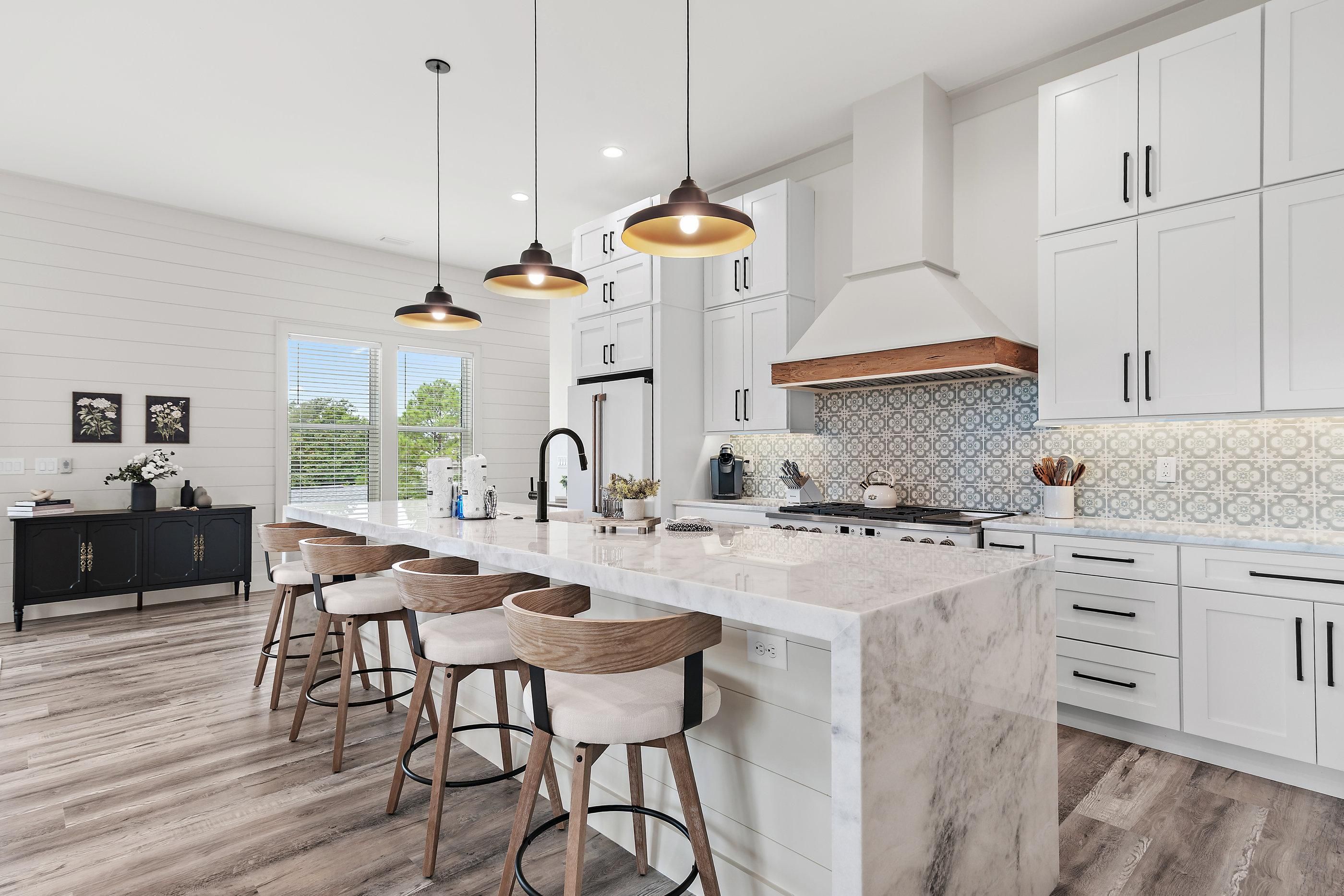 A modern kitchen with a large island, pendant lighting, and a view to the outdoors.