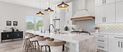 A modern kitchen with a large island, pendant lighting, and a view to the outdoors.