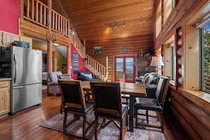 A spacious wooden cabin interior with a dining area, kitchen, and a cozy seating area with a fireplace. - Nordic By Nature | Fireplace |  Playset | Fire Pit (Eden)