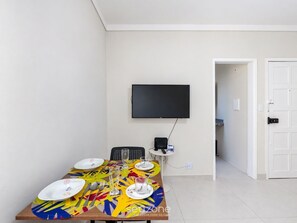 A dining area with a table set for four, a flat-screen TV mounted on the wall, and a door leading to another room. - Well-located Apt. in Pituba Azs0201 (Salvador)