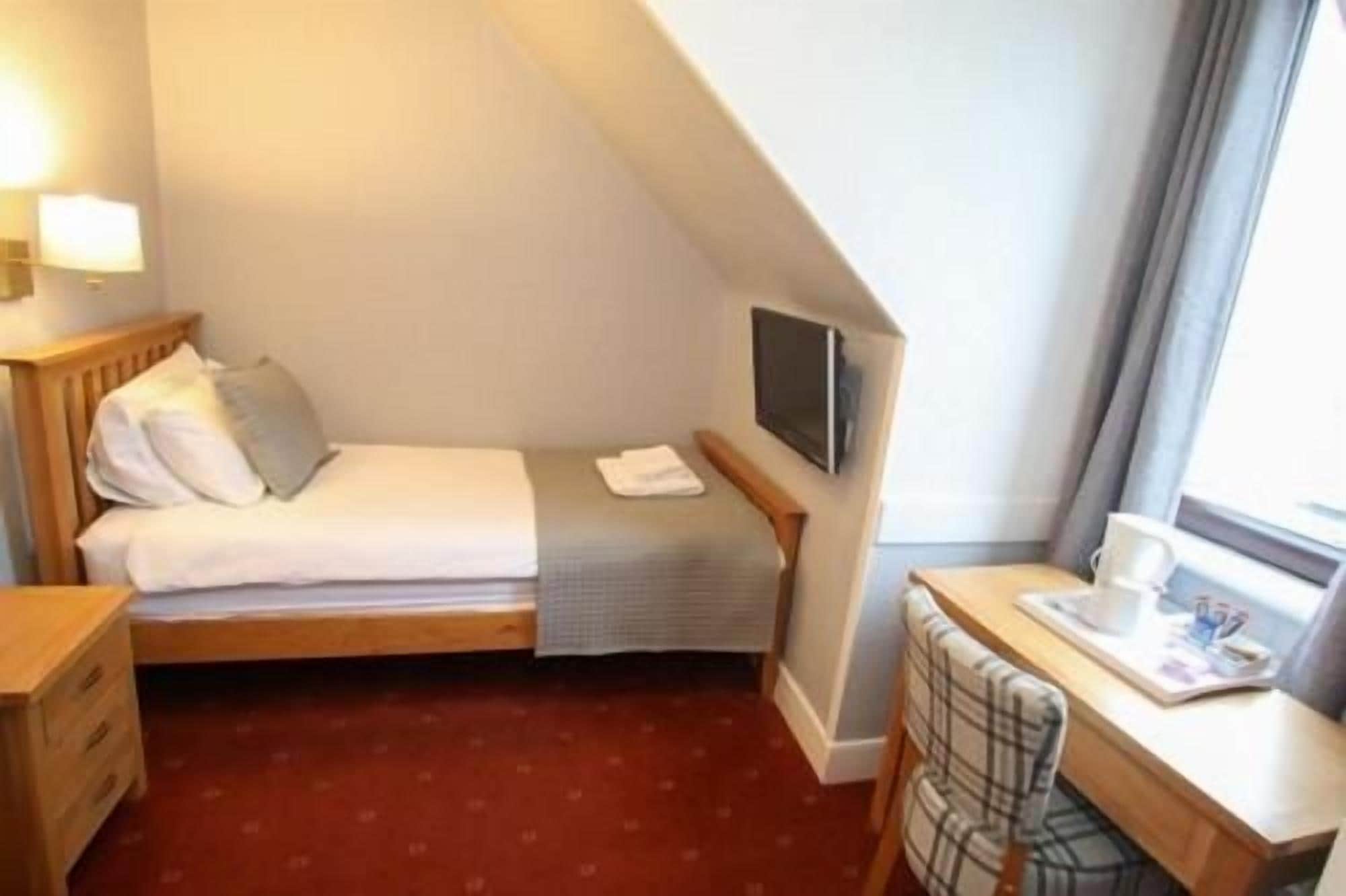 A small, single-bed room with a desk and chair, a television, and a window with curtains.