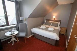 A hotel room with a bed, bedside table, chair, and a window.