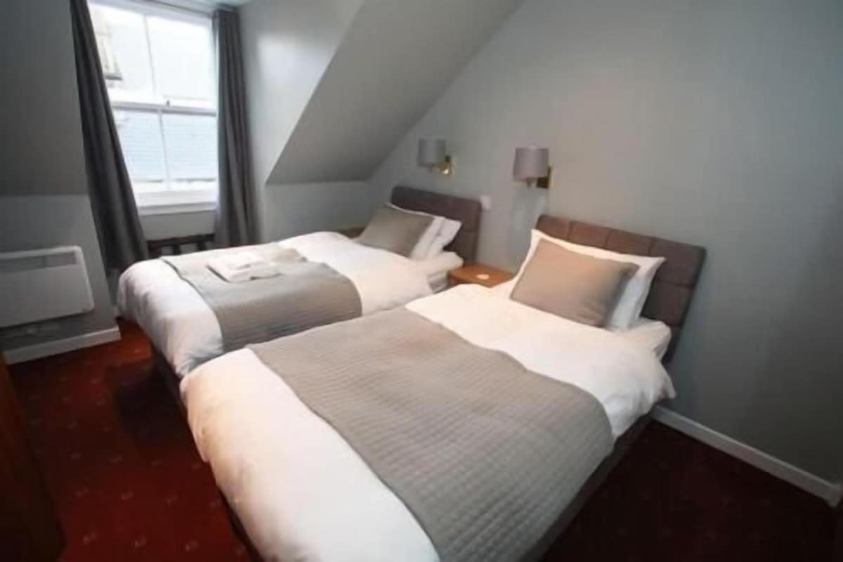 A hotel room with two beds, a window, and a radiator.